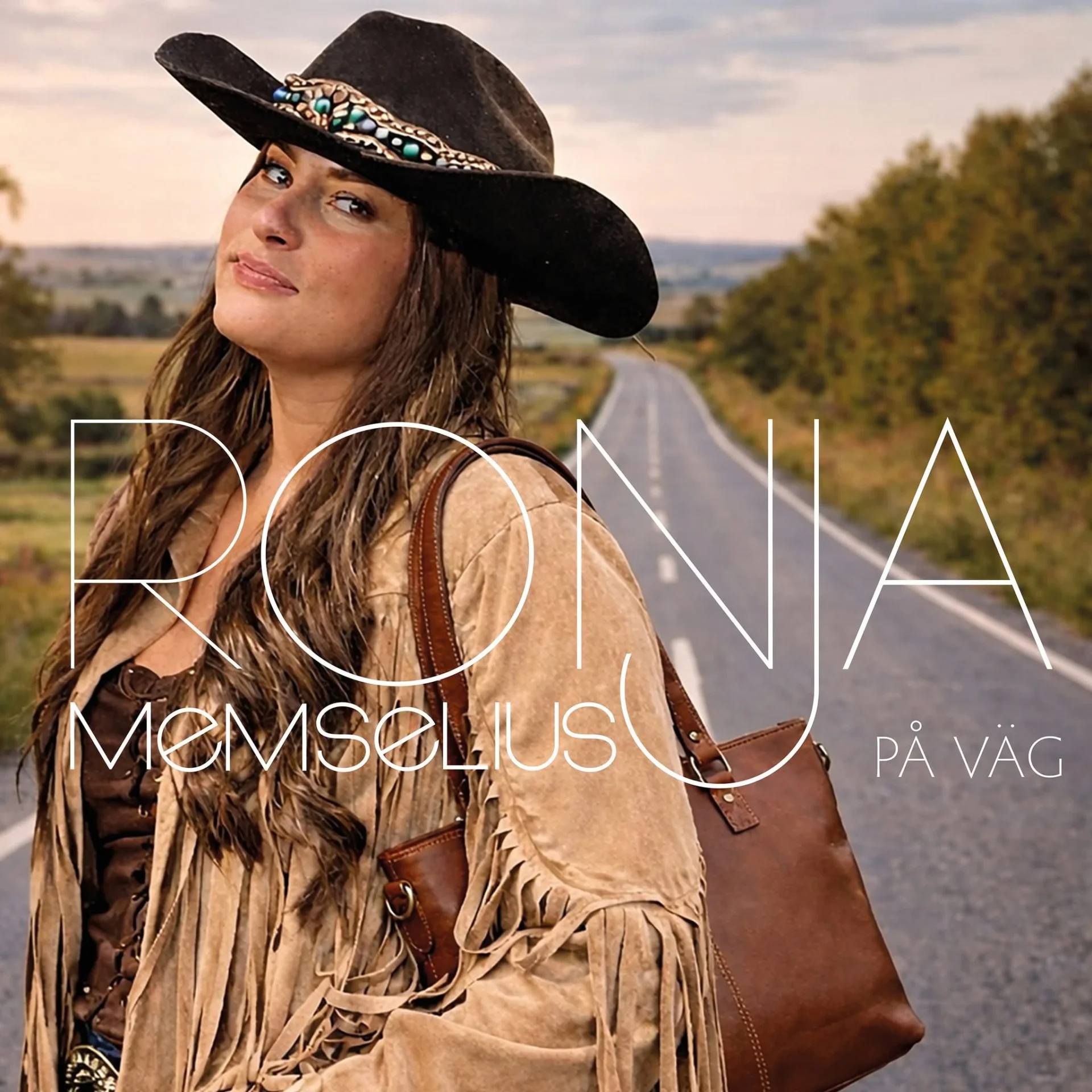 Omslaget för Ronjas CD. Ronja vänd mot vänster sida klädd i kläder av western-stil och bärandes på en läderväska. Bilden innehåller texten "Ronja Memselius På Väg".